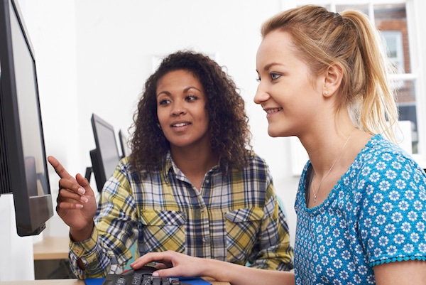 Two people sitting at a computer, one person pointing to the screen and the other one operating the mouse.