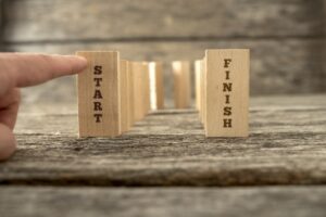 Dominos standing in U shape with the ending ones holding the words Start and Finish and a finger about to knock down the first one