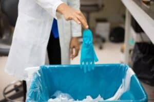 Closeup image of healthcare professional throwing away blue disposable gloves in trash.