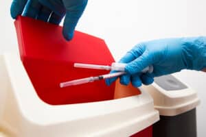 The nurse throw away used syringe into red bin